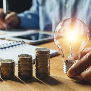 a person holding a lightbulb next to some coins while doing invoices