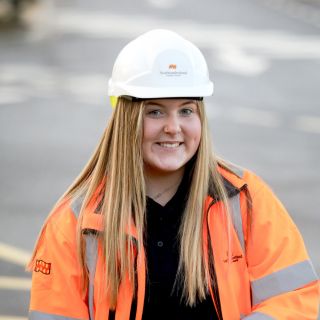 Young woman with blonde hair wearing a hard had and hi-viz jacket smiling at the camera