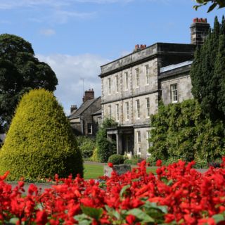 Hexham house on a sunny day with blue skies and red flowers in the foreground