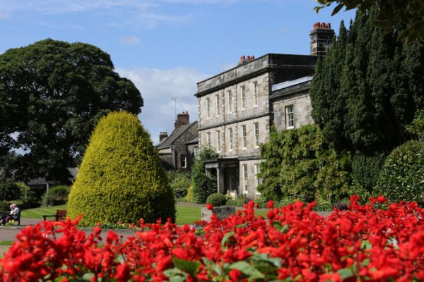 Hexham house on a sunny day with blue skies and red flowers in the foreground
