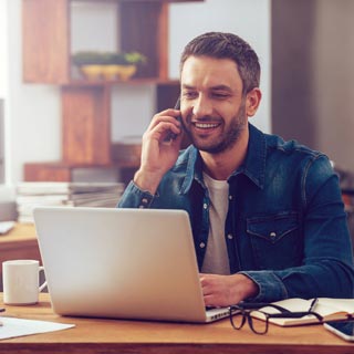 A young man on a laptop while contacting someone on a phone