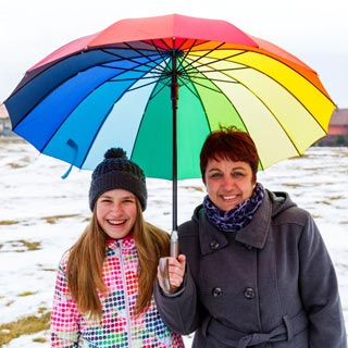 A foster parent and child under a rainbow umbrella