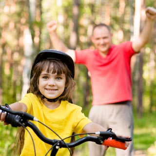 A young child riding a bike with a foster parent cheering behind them