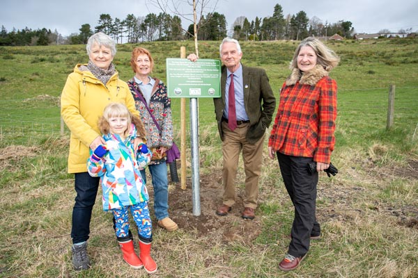 Councillor Glen Sanderson at a plaque for tree wardens surrounded by a group of wardens and trees.