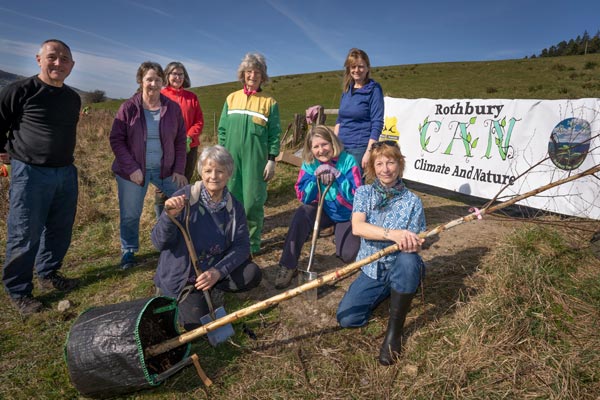 The group Rothbury Climate and Nature all standing around a tree sapling innn a open field with shovels ready to plant some trees.