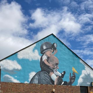 A mural painting on the side of a house. It is of a grandparent and a young child with a miner's helmet on looking at a bird.