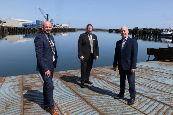 Three men standing on the harbour in the Port of Blyth by the river mouth.