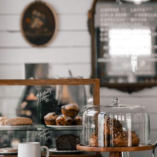 A cafe bench with cakes and coffee on display with a menu on the wall in the background