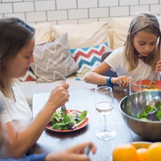 A family having dinner. A mother and young daughter are eating a salad with water to drink