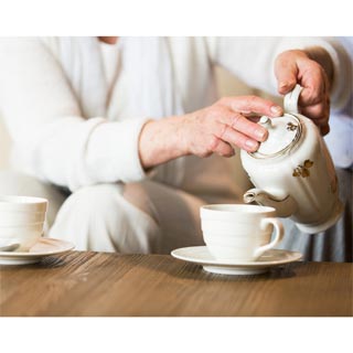 An elderly person pouring a cup of tea