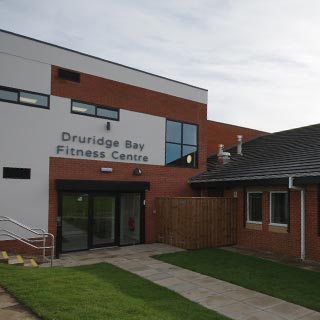 Outside of Druridge Bay Fitness Centre, a brick building with a glass door.