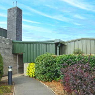 The outside of Rothbury leisure centre, a green metal building surrounded by hedges.