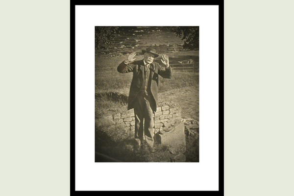 Sepia image of photographer J.P. Gibson standing on Hadrian's Wall with his hands raised. 