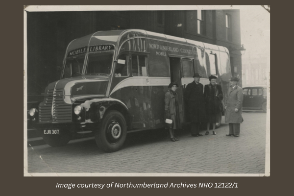 A black and white image of the first mobile library purchased in 1951. There are four people standing in front of the vehicle. 