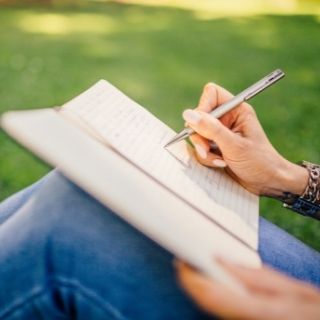 Person sitting on grass writing in a notebook