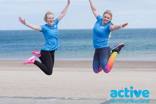 Two people jumping in the air with Active Northumberland t-shirts on