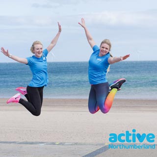 Two people jumping in the air with Active Northumberland t-shirts on