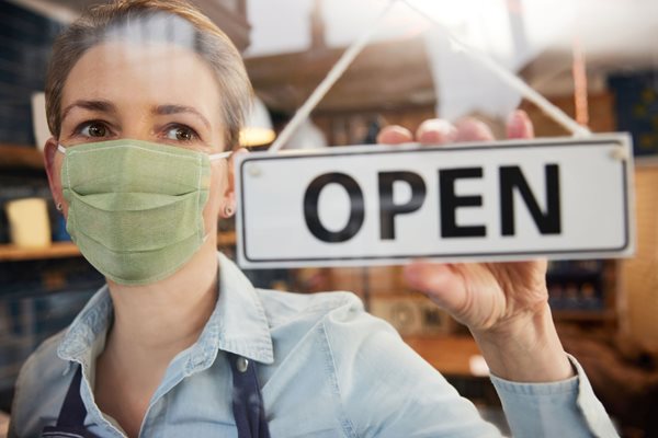 Photo of woman in mask turning Open sign