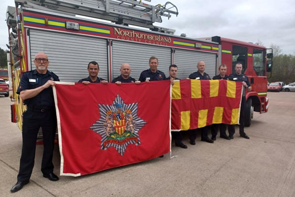 A group of Northumberland Fire and Rescue Firefighters standing in front of a fire engine with the NFRS and Northumberland County Flag. The photo was taken at their destination of Ukraine.