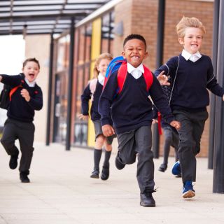 A group of school children in uniform running and smiling 