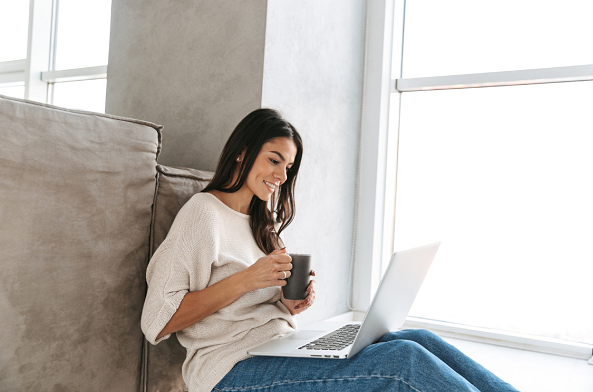 A woman enjoying a hot drink while looking at her laptop