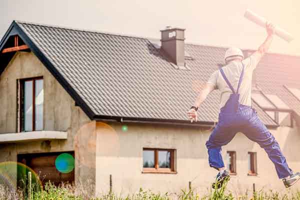 A builder jumping in the air in front of a new house