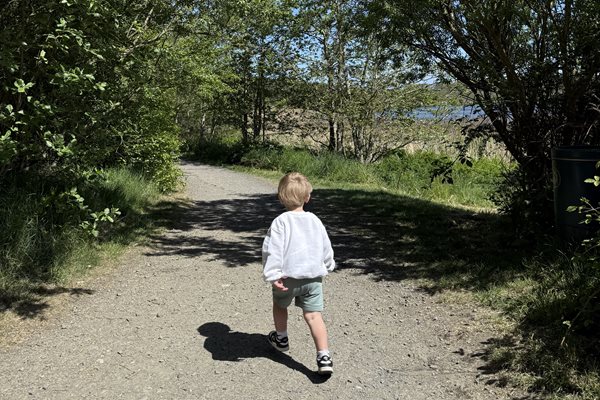 A little boy exploring Druridge Bay Country Park- image taken from the back, with lake in the background