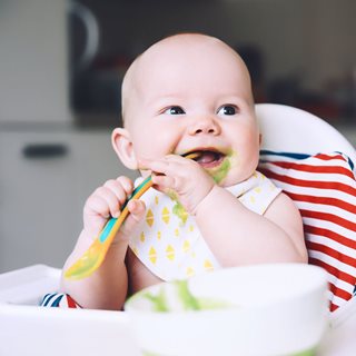 Baby laughing and trying to feed itself with baby food