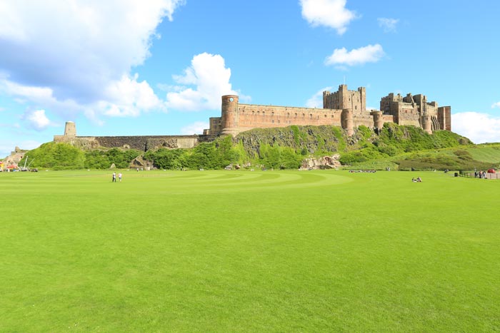 Bamburgh castle in the bright sun, with the green field below with people walking around
