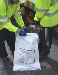 Two workers filling a bag of road samples