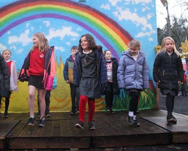 A group of school children smiling while clog dancing on a stage